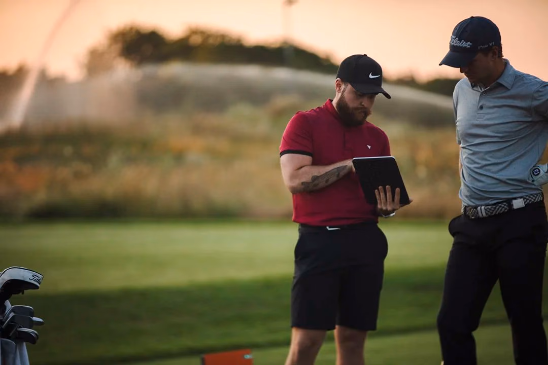 Un enseignant et un golfeur consultent ensemble une tablette près du practice.