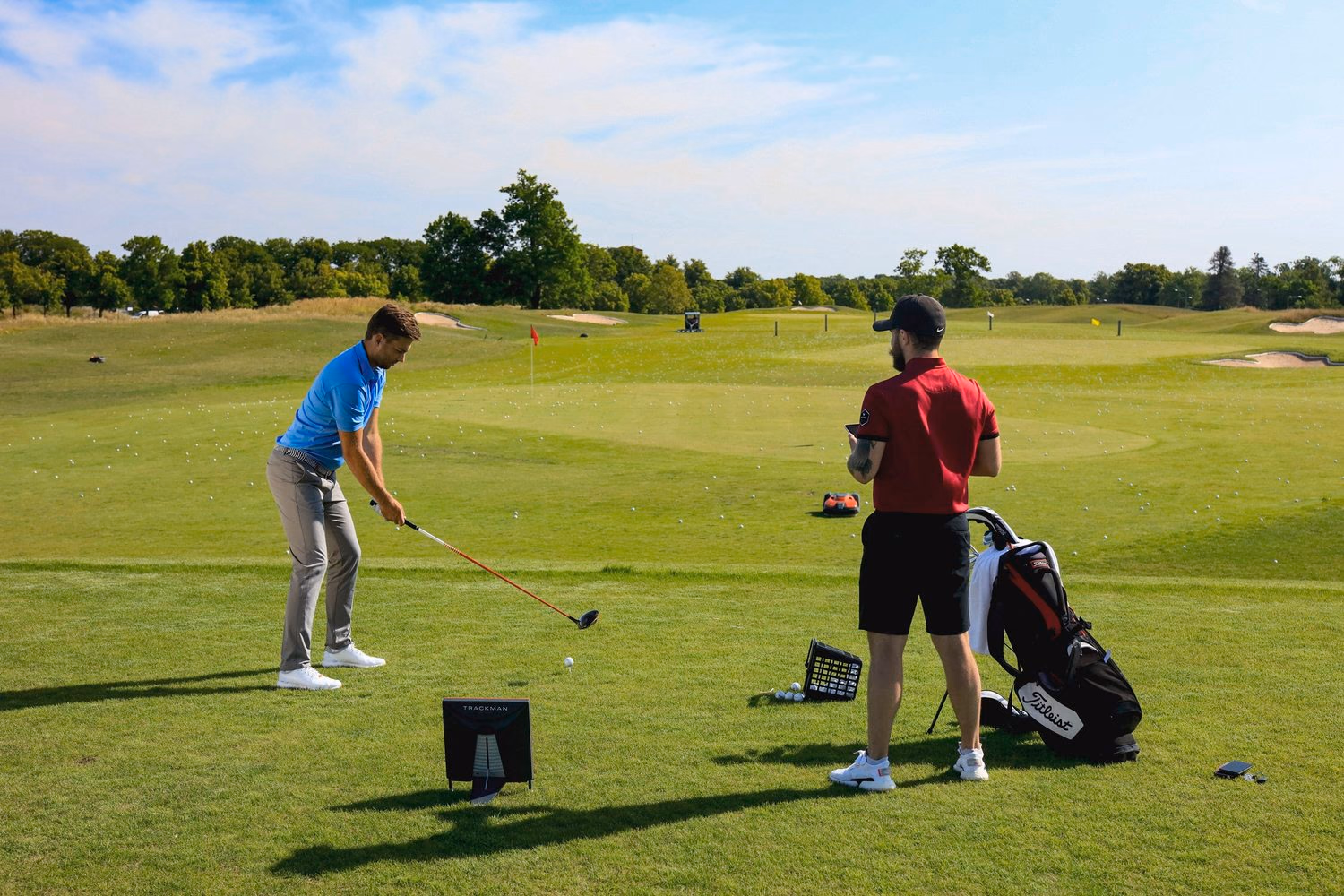 Un golfeur prépare son coup au practice pendant que son enseignant tient une tablette.